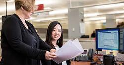 Female intern reviews a document handed to her by another female.